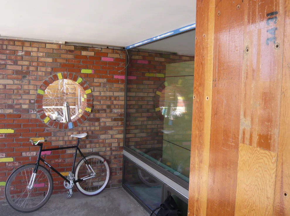Brick wall with circular window and large glass window adjacent to a wooden panel.