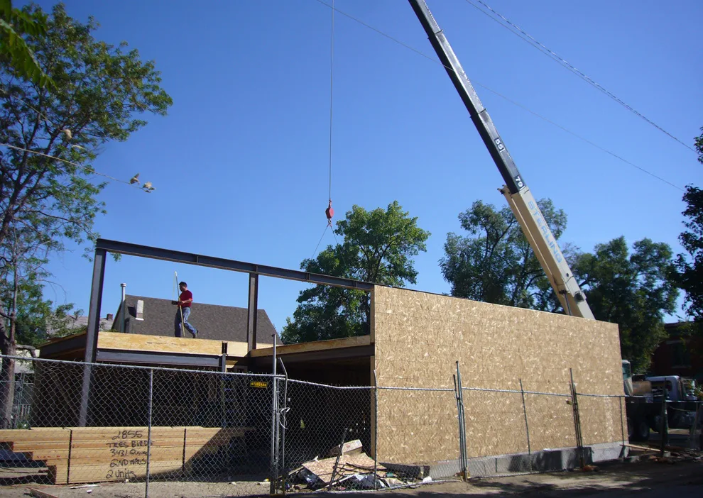 Steel frame structure under construction with OSB sheathing and a worker on site.