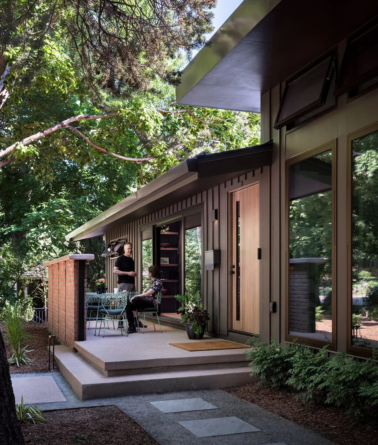 A mid-century modern exterior with a wood front door and brick wall on the patio of the V|O Residence in Denver.