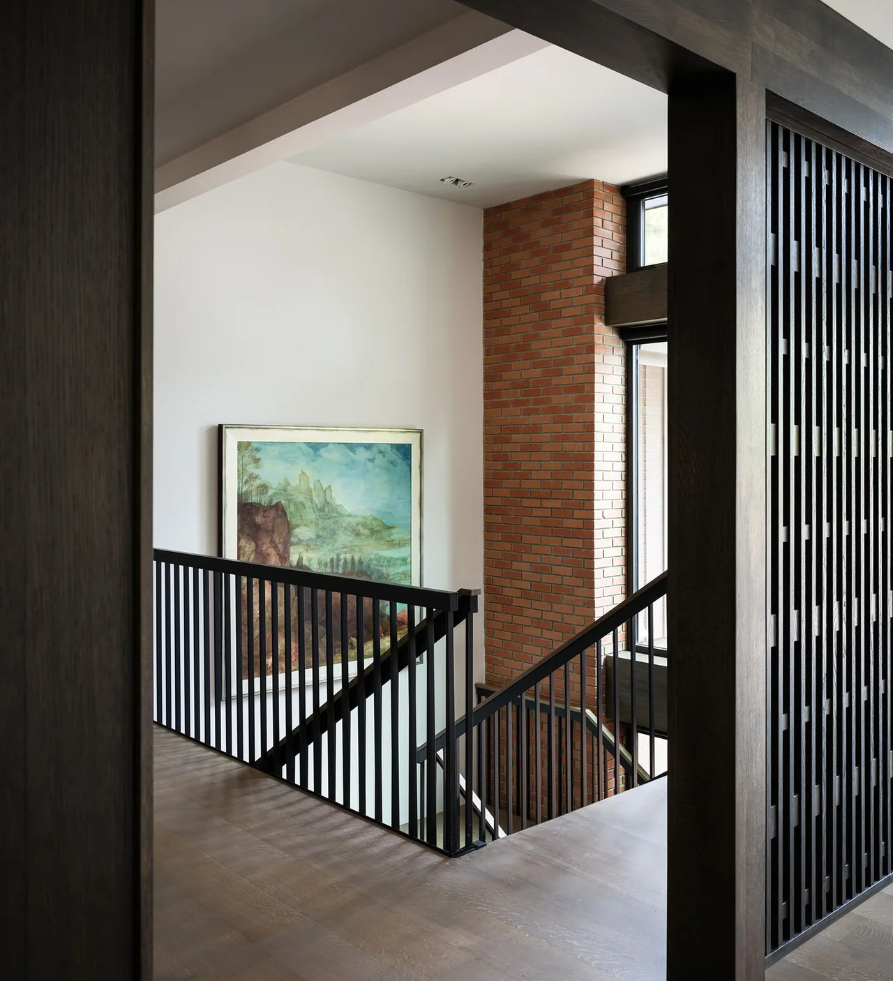 The stairwell features a black vertical wood slat railing adjacent to a red brick accent wall with windows.