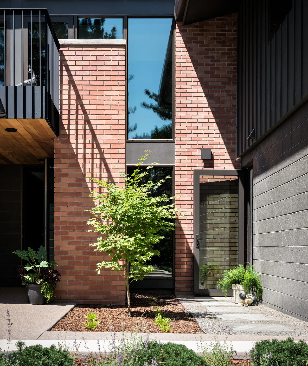 The V|O Residence courtyard features red brick walls with floor-to-ceiling glazing and a black-framed glass door.