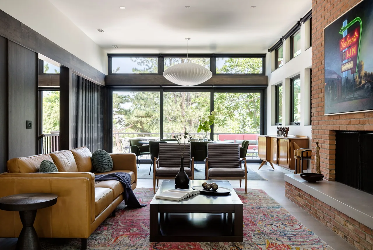 Living and dining room of V|O Residence featuring floor-to-ceiling windows and a brick fireplace.