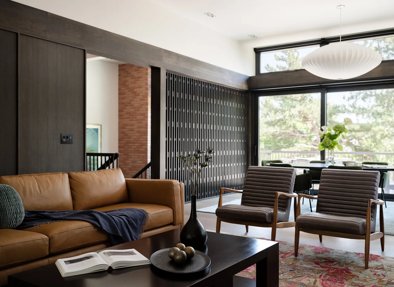 Living area of V|O Residence features modern furniture and a dark wood slat divider wall under large windows.