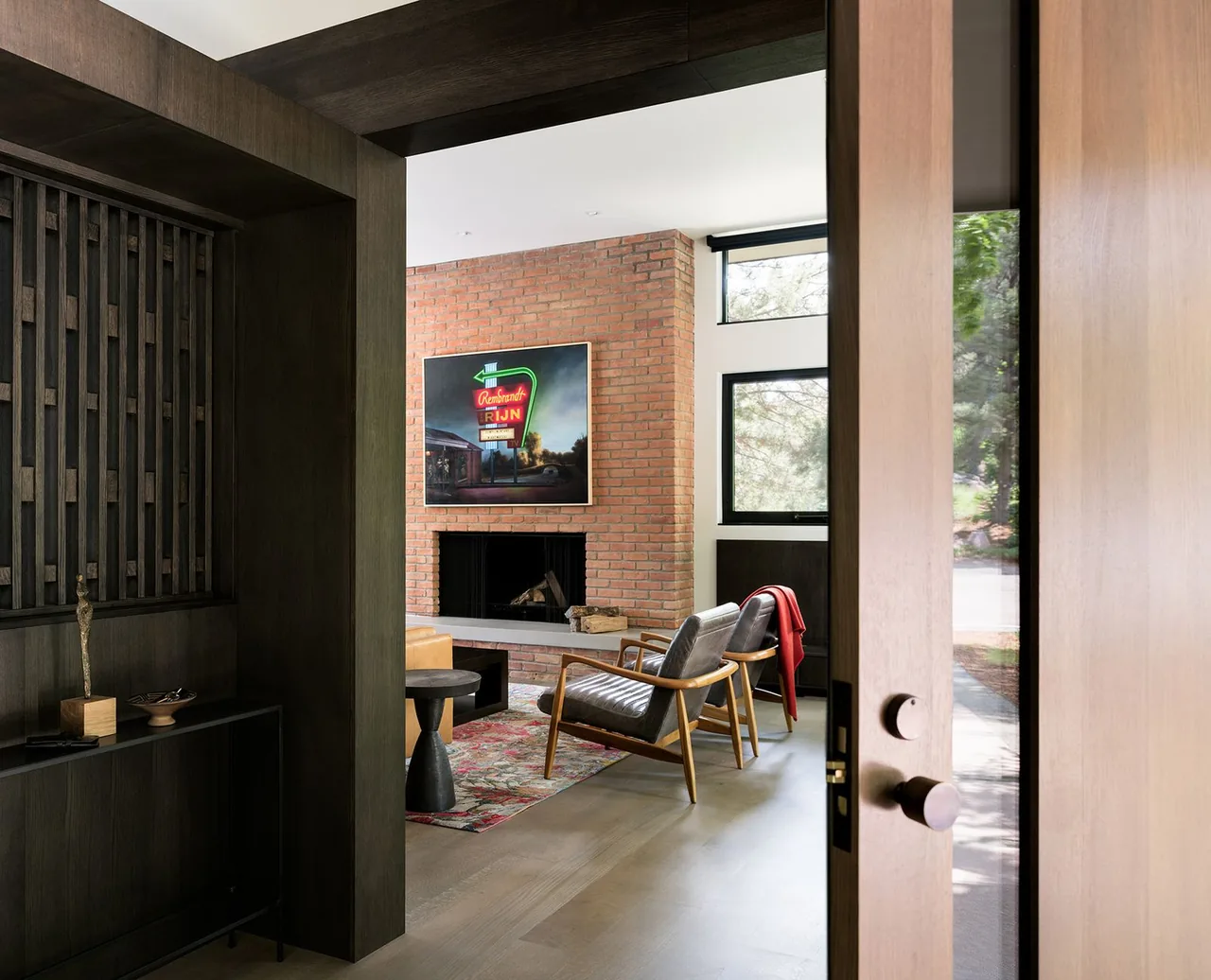 Living room with a brick fireplace, two armchairs, and a patterned area rug seen through an open entry door.