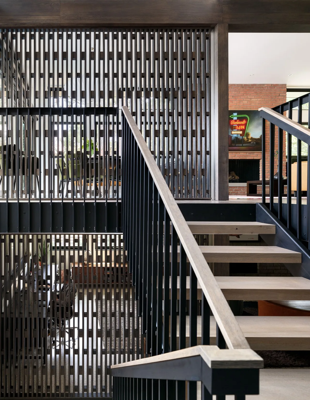 The staircase features wood treads and black metal railings beside a decorative wood slat divider, with a brick fireplace visible in the background.