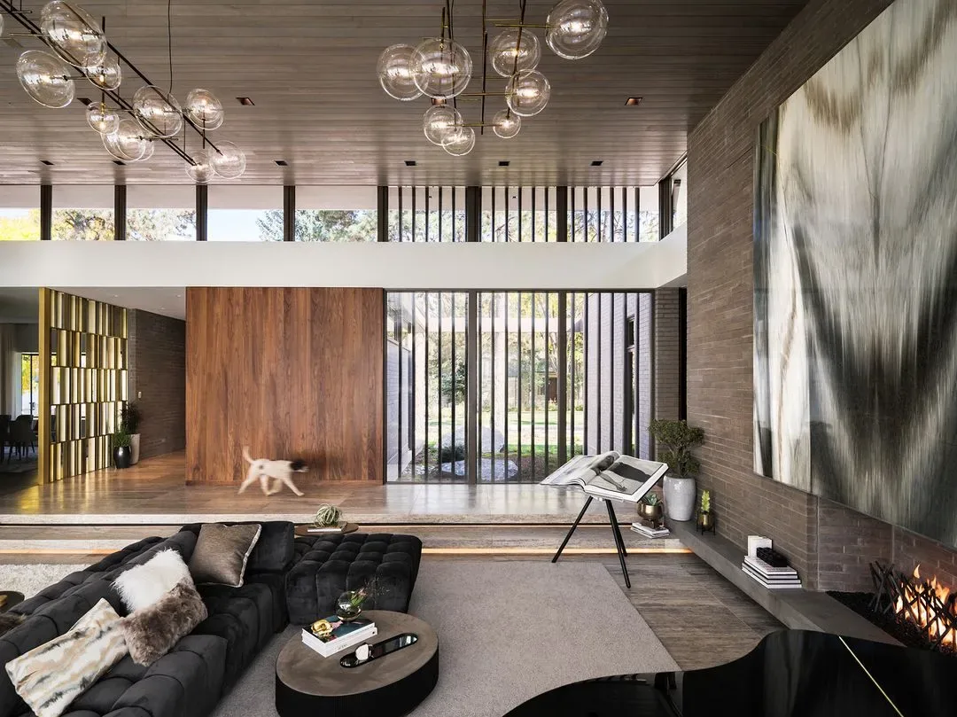 Living room features large floor-to-ceiling windows, wood-paneled ceiling, and a fireplace with abstract art above it.
