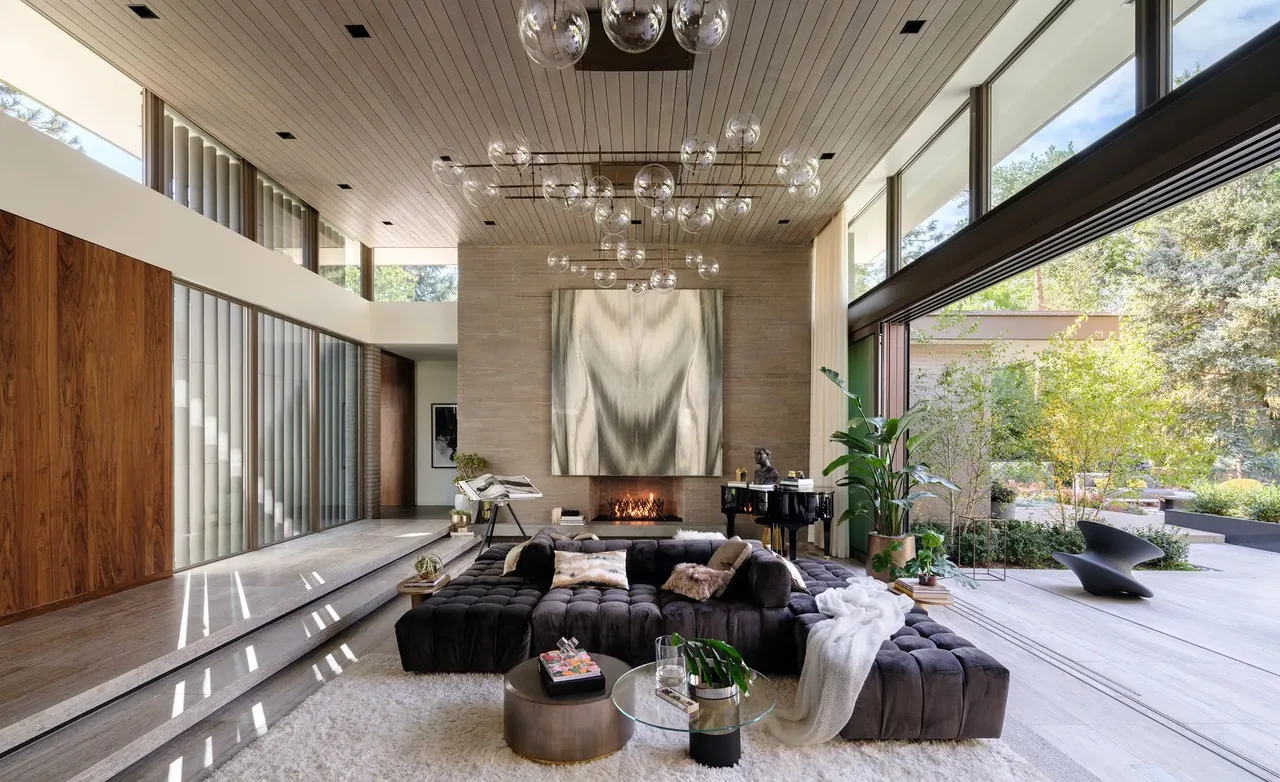 Modern living room with floor-to-ceiling windows, a fireplace, and dark tufted sectional sofa connected to an outdoor patio.