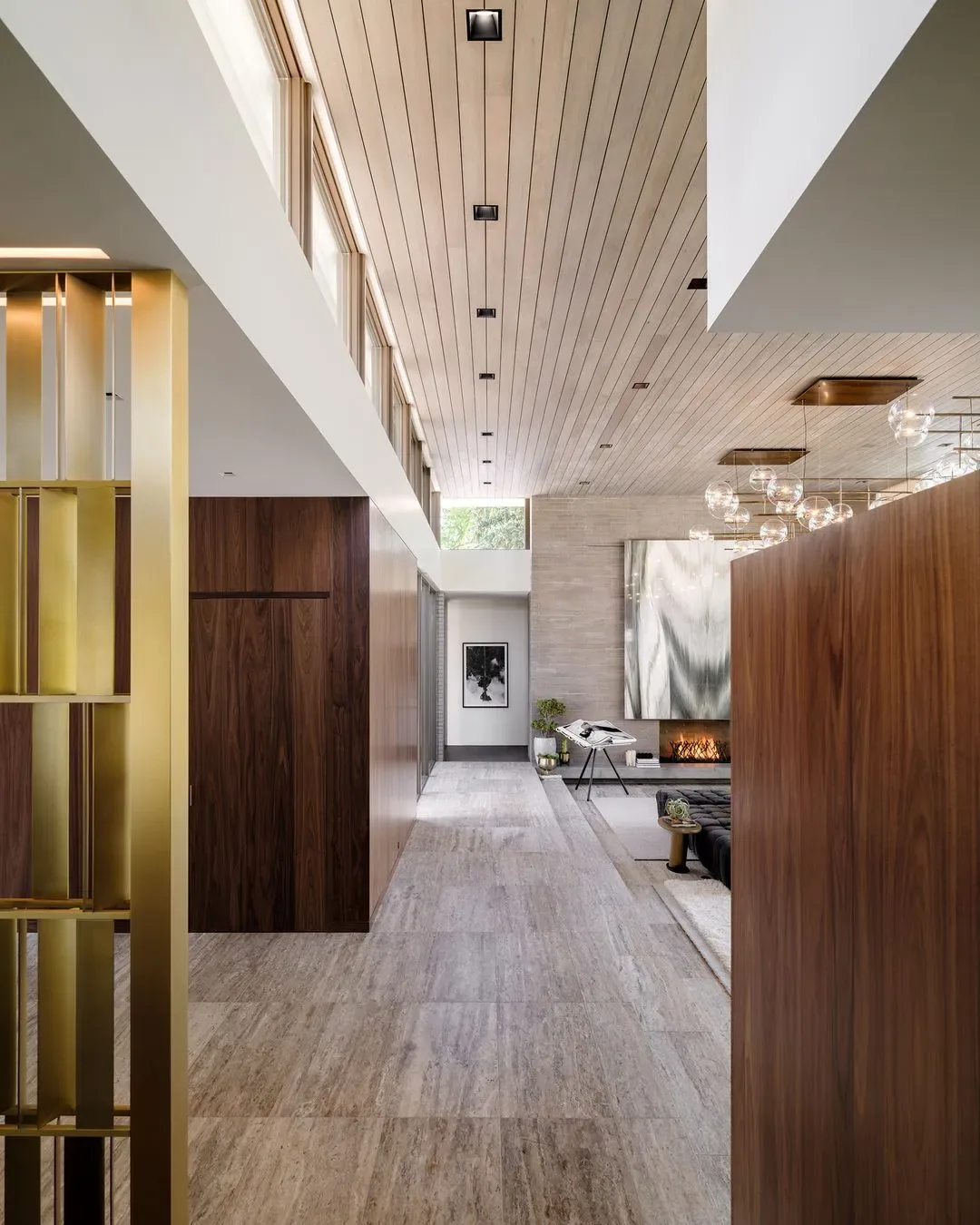 View looking down a hallway with wood ceiling, stone tile floor, wood paneled walls, and a fireplace.
