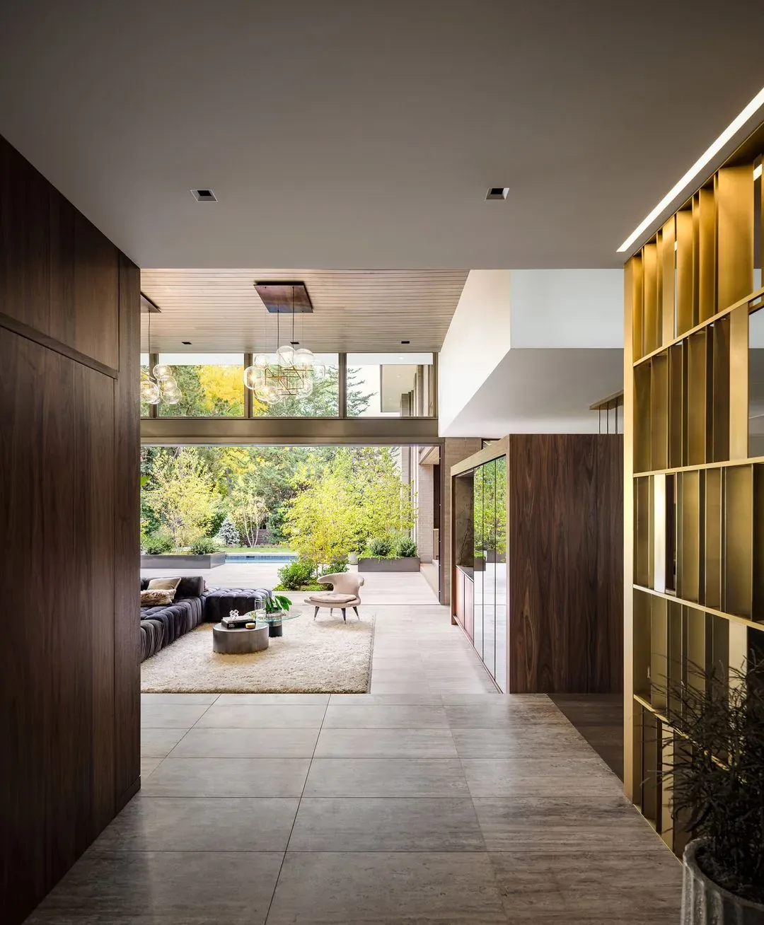 Interior view looking from hallway into living room with floor-to-ceiling glazing and outdoor landscape visible.