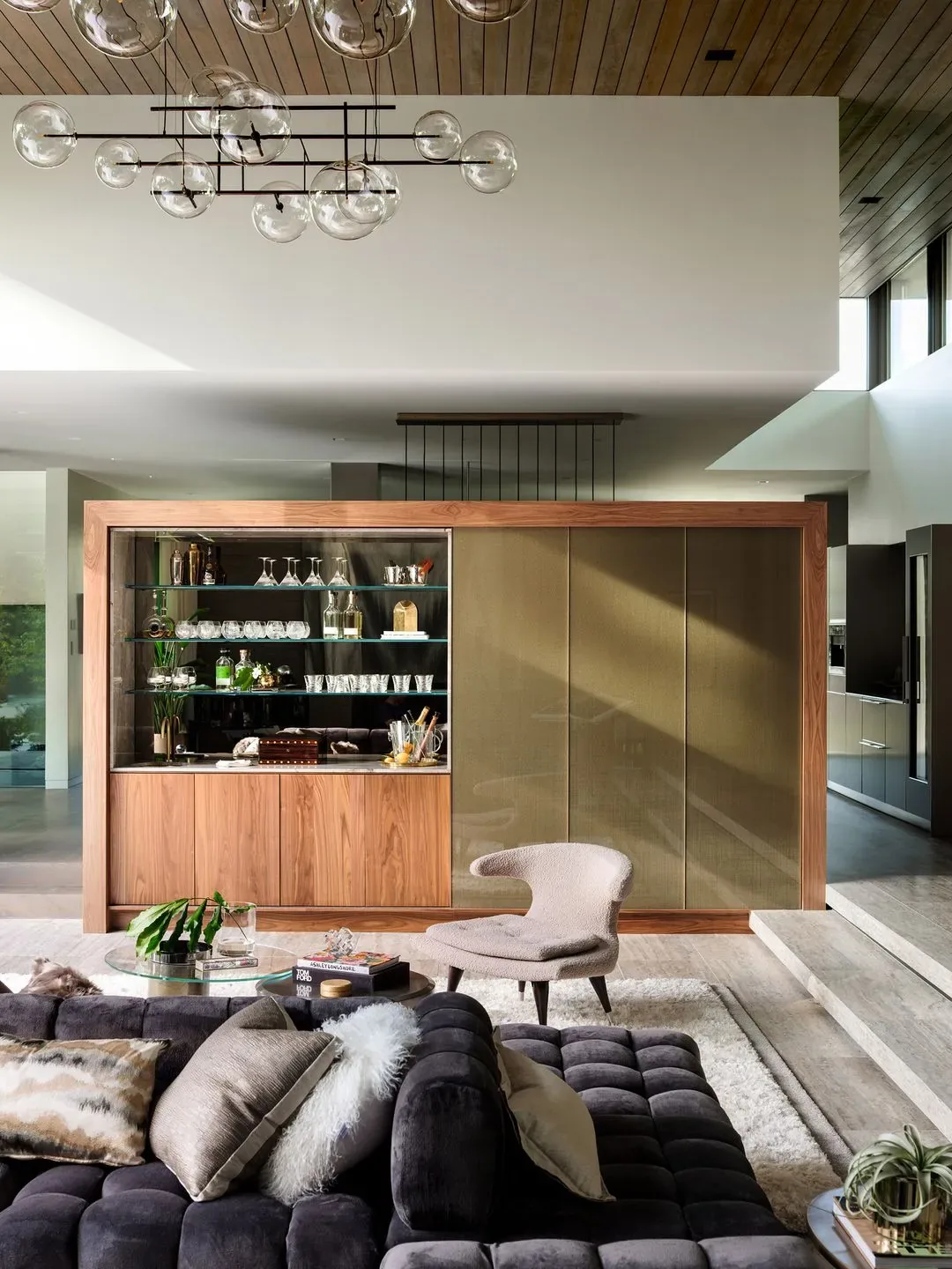 Living room features wood paneling, glass shelving in bar cabinet, and a modern pendant light fixture.