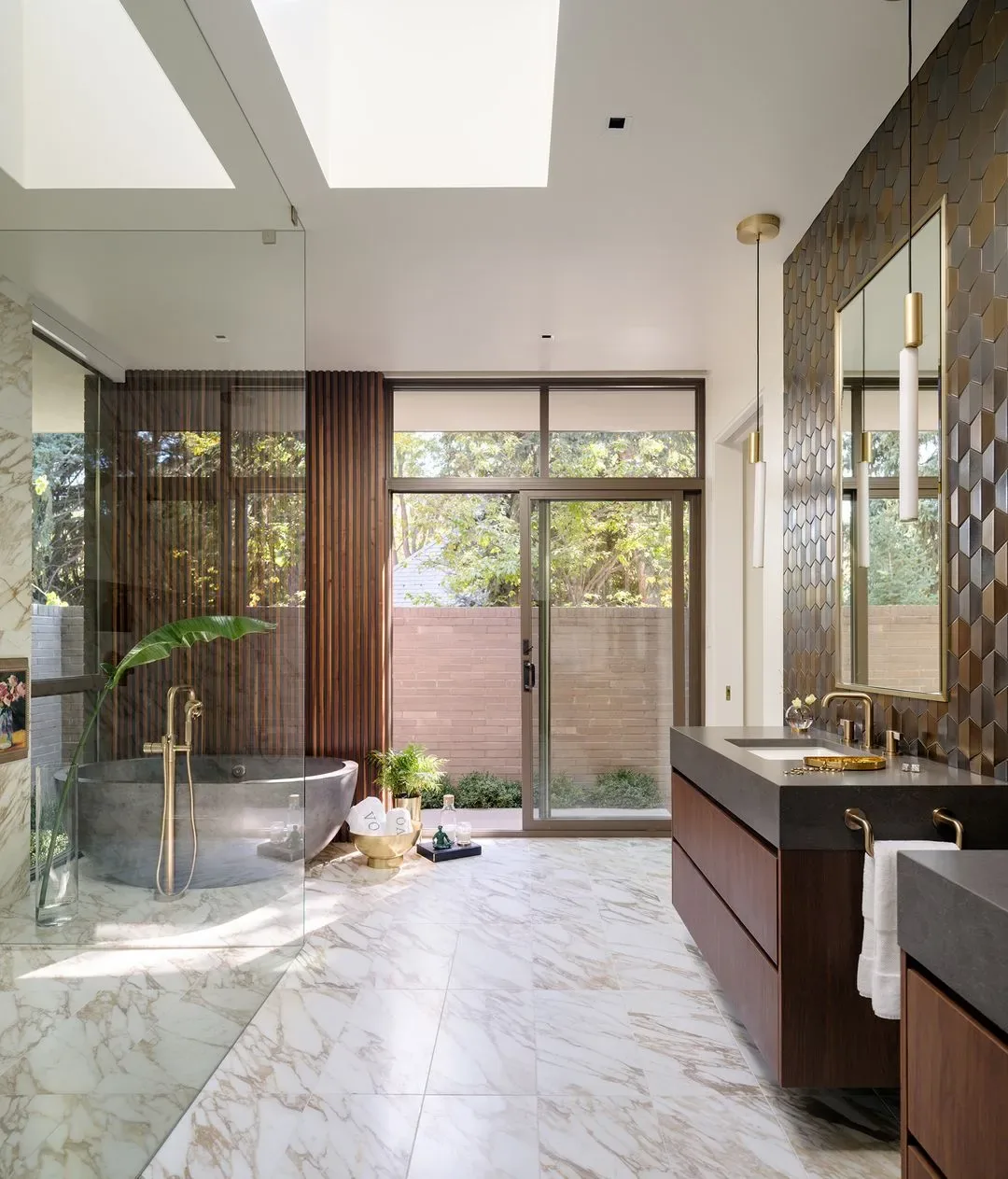 Bathroom with marble tile floor, freestanding tub, large window, and wooden vanity with brass fixtures.