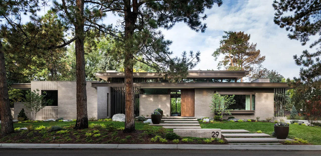 Front view of a modern flat-roofed brick house with a wooden entrance door and landscaped yard with stepping stone pathway.