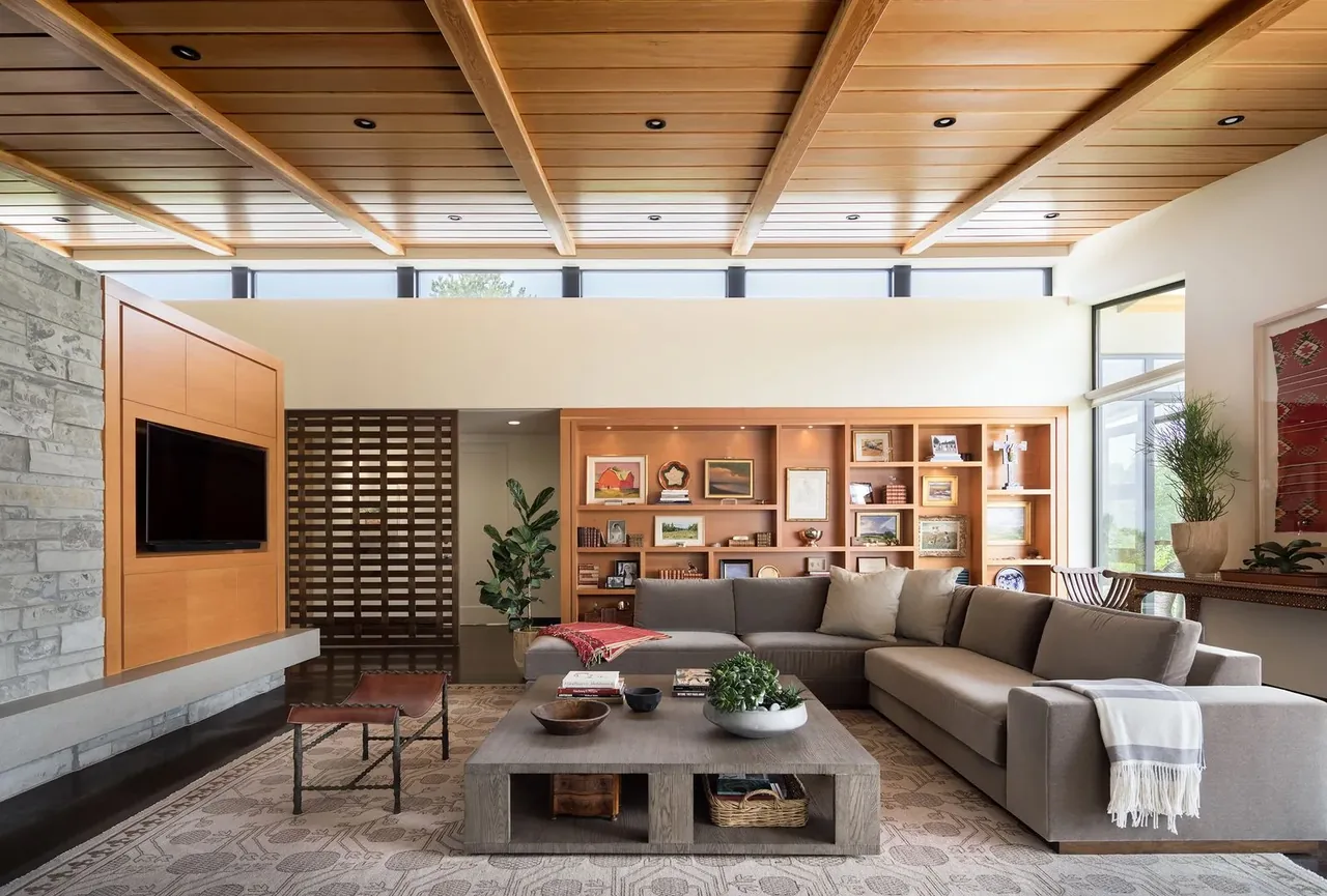 Living room with wood-paneled ceiling, clerestory windows, built-in shelving, and a stone fireplace surround.
