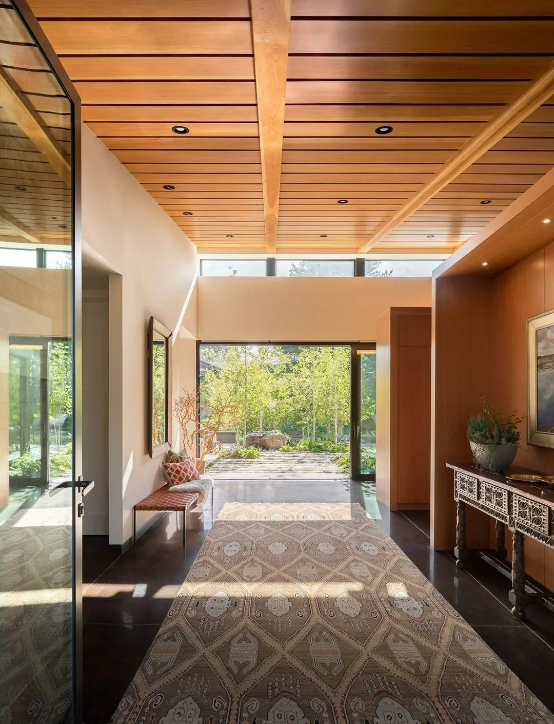 Entry hallway of the Cherry Residence features a wood-paneled ceiling and large glass door opening to the garden.