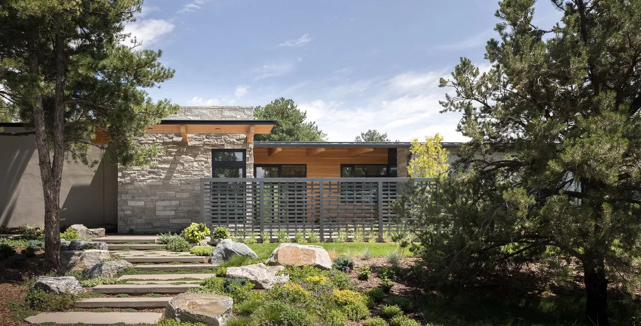 Exterior view of Cherry Residence featuring stone cladding, wood soffits, and a metal privacy screen with natural landscaping.