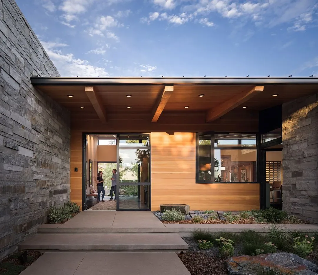The Cherry Residence exterior features stone cladding, wood siding, and a flat roof with recessed lighting over the entry.