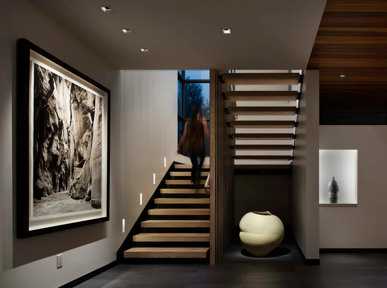 Modern floating wooden stair with picture window and recessed wall lighting in a double height space.