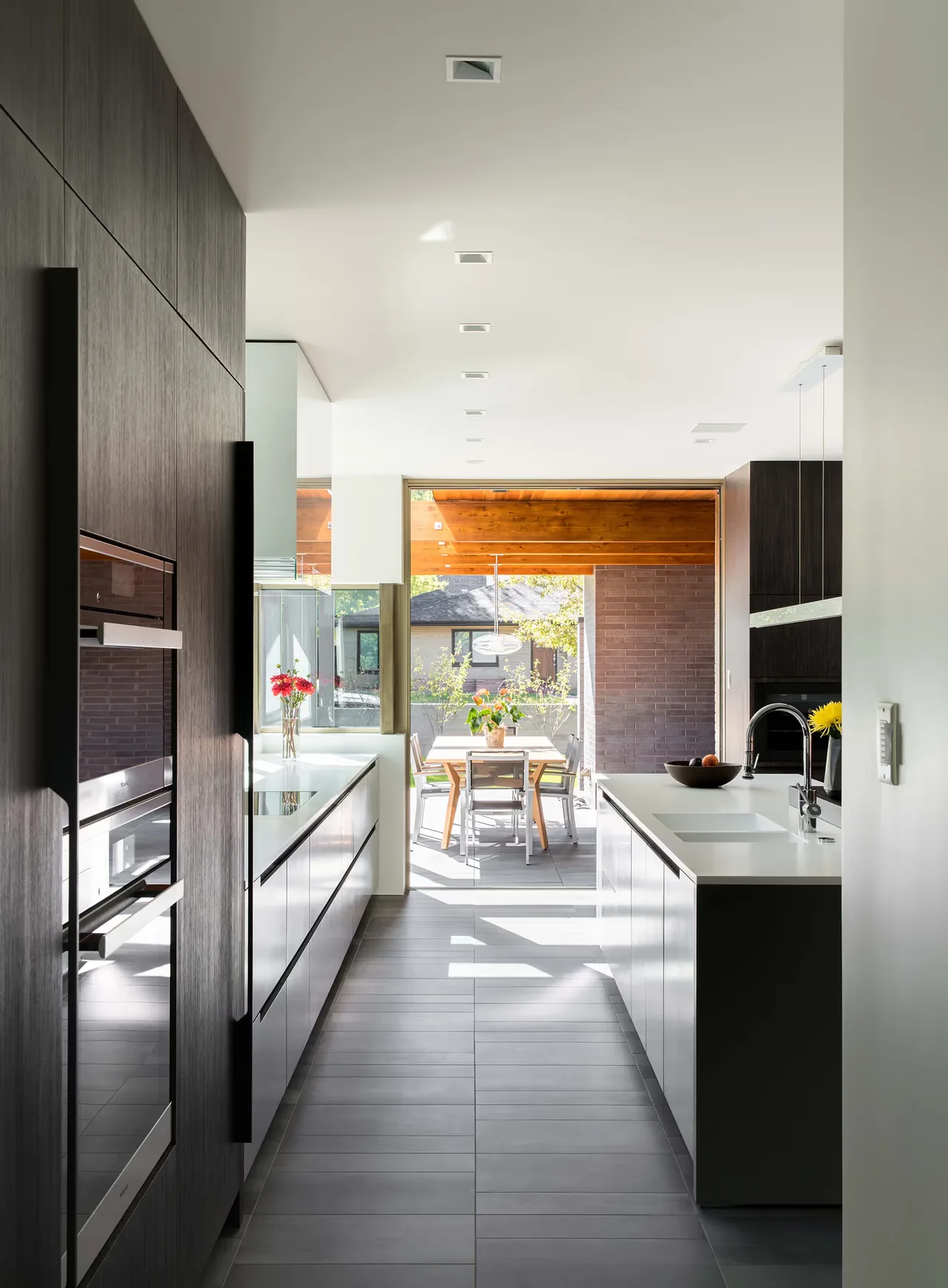 The Duncan Residence kitchen features dark wood cabinets, white quartz counters, and a dining area with large sliding glass doors to the outside.