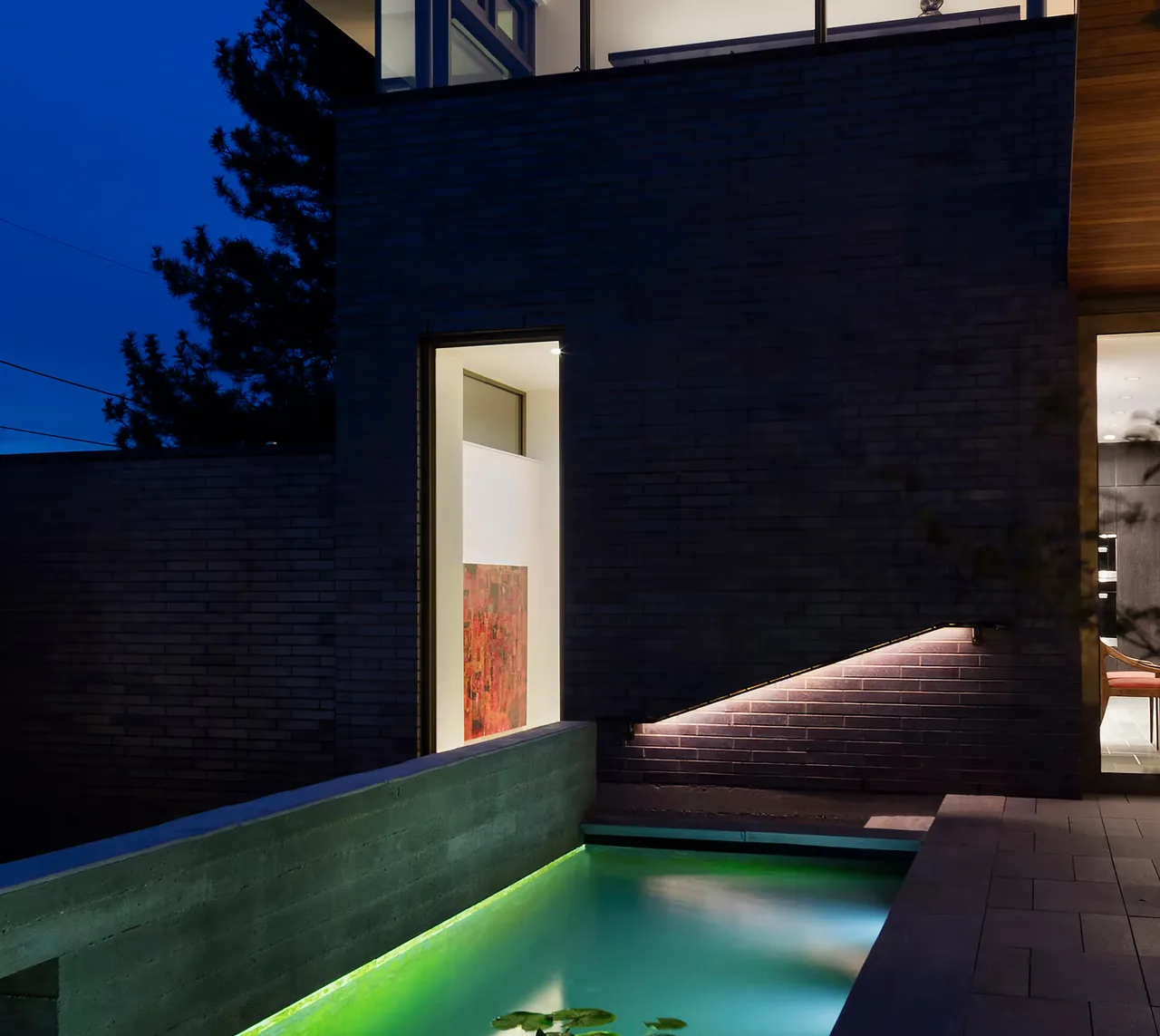 The Duncan Residence exterior features a cantilevered brick wall over a pool illuminated by integrated lighting.