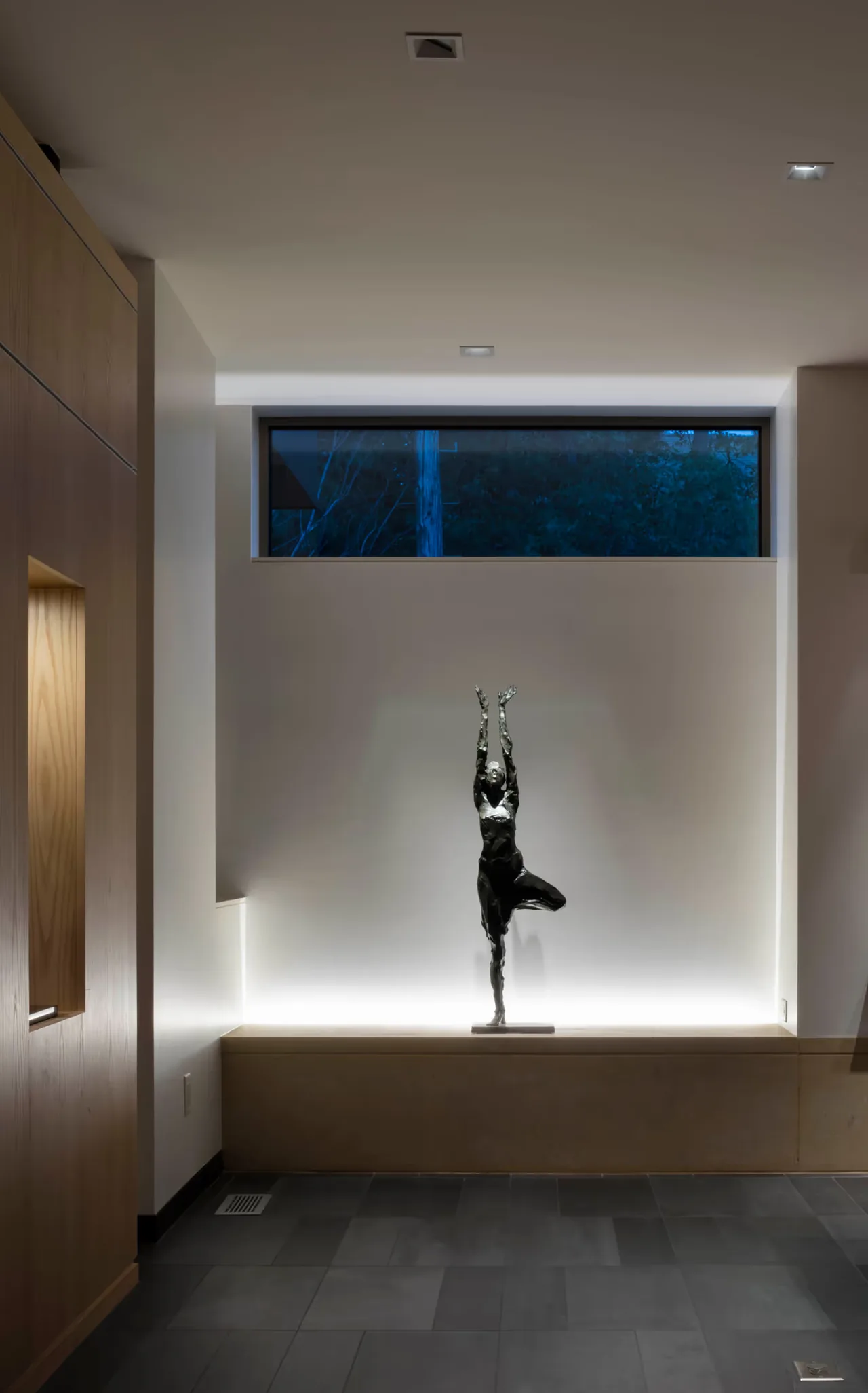 Interior niche features a black dancer statue backlit with concealed lighting under a clerestory window.