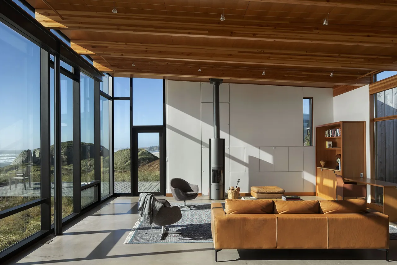 The living room features floor-to-ceiling glazing, a wood-paneled ceiling with exposed beams, and a freestanding stove.