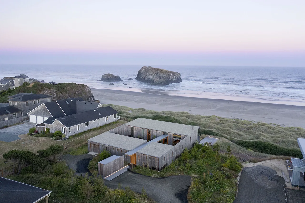 Modern beach house with flat roof and wood siding situated near sandy dunes on the Oregon coast.