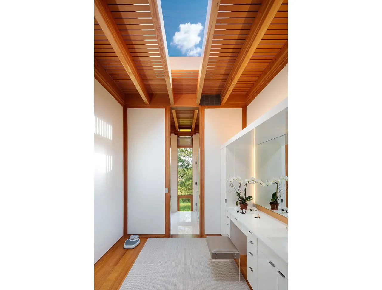 Bathroom interior featuring wooden beams, a skylight, and a long vanity with a mirror and orchids.