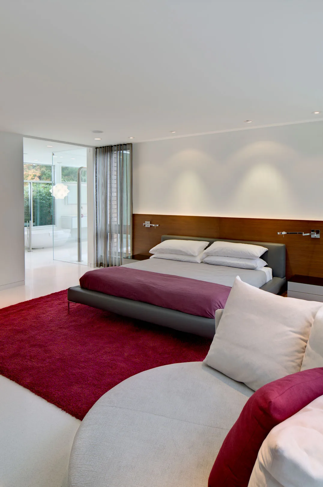 A modern bedroom with recessed lighting and glass partition leading to a bathroom area.
