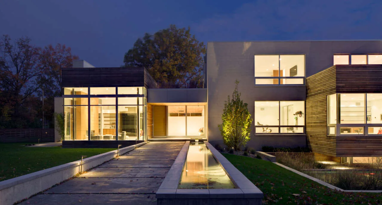 Exterior front view of the Shaker Heights Residence illuminated at dusk with extensive glazing and wood siding.