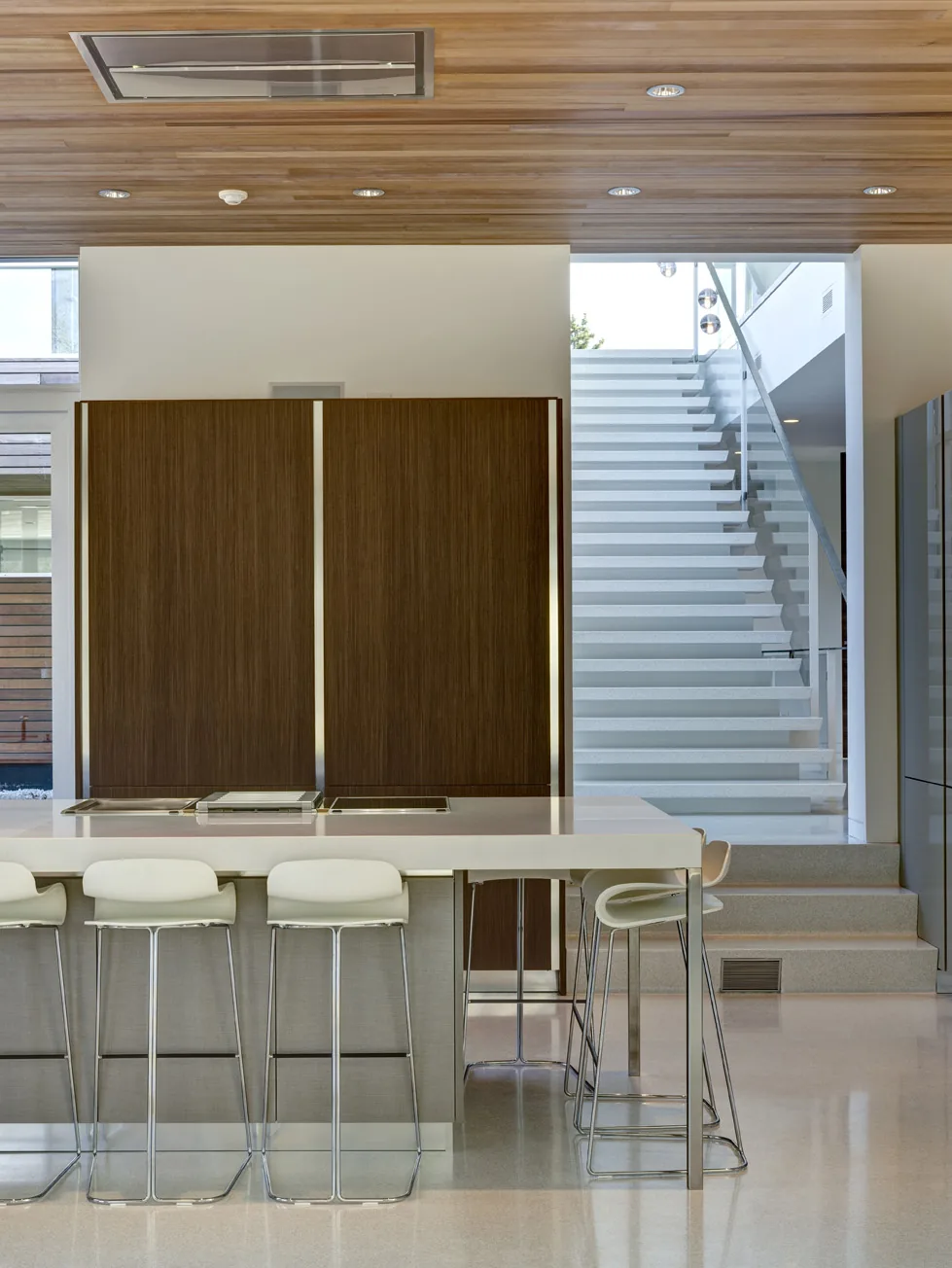 The kitchen island with seating and a white staircase with a glass balustrade in the background.