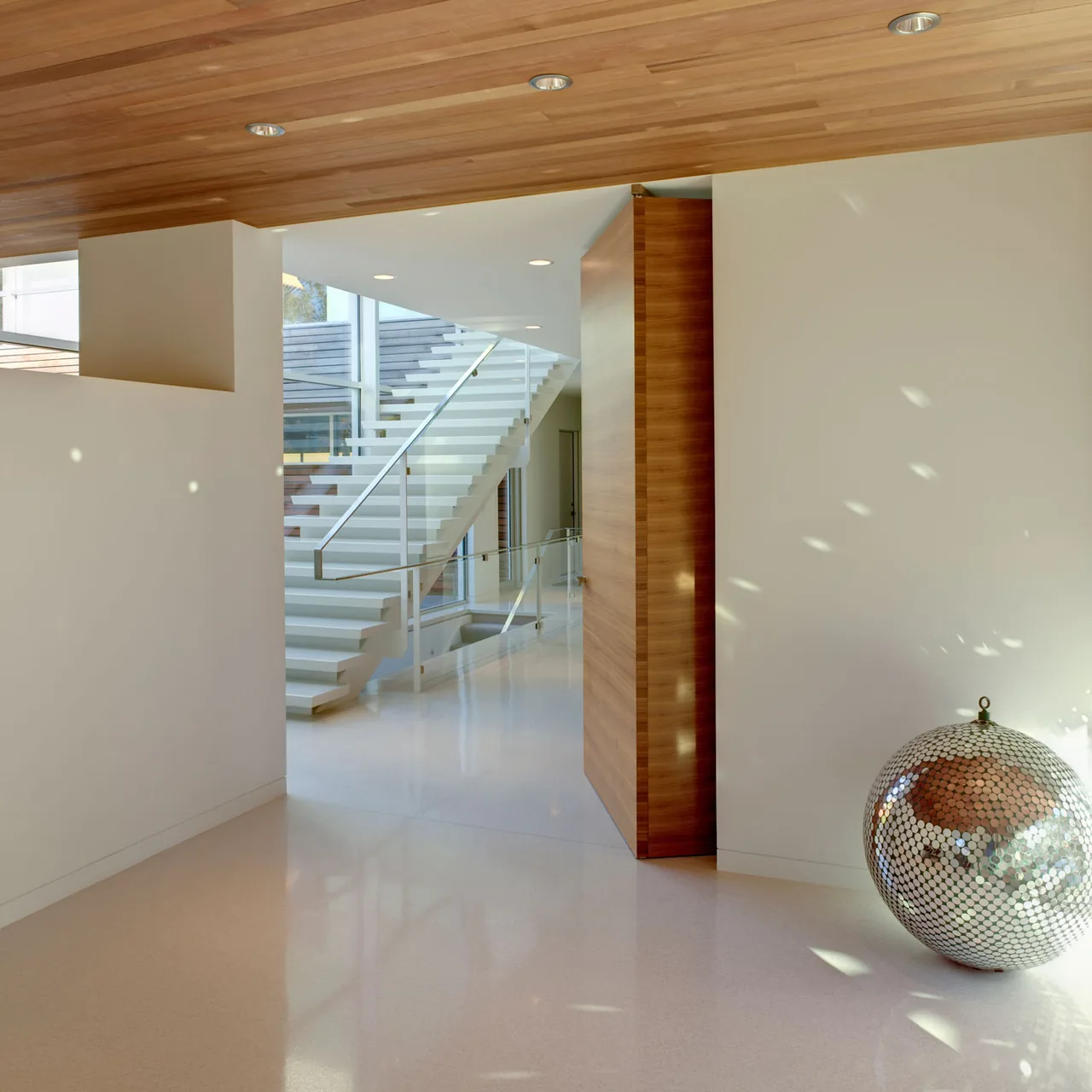 White floating staircase with glass railing in a modern interior with wood accents and terrazzo flooring.