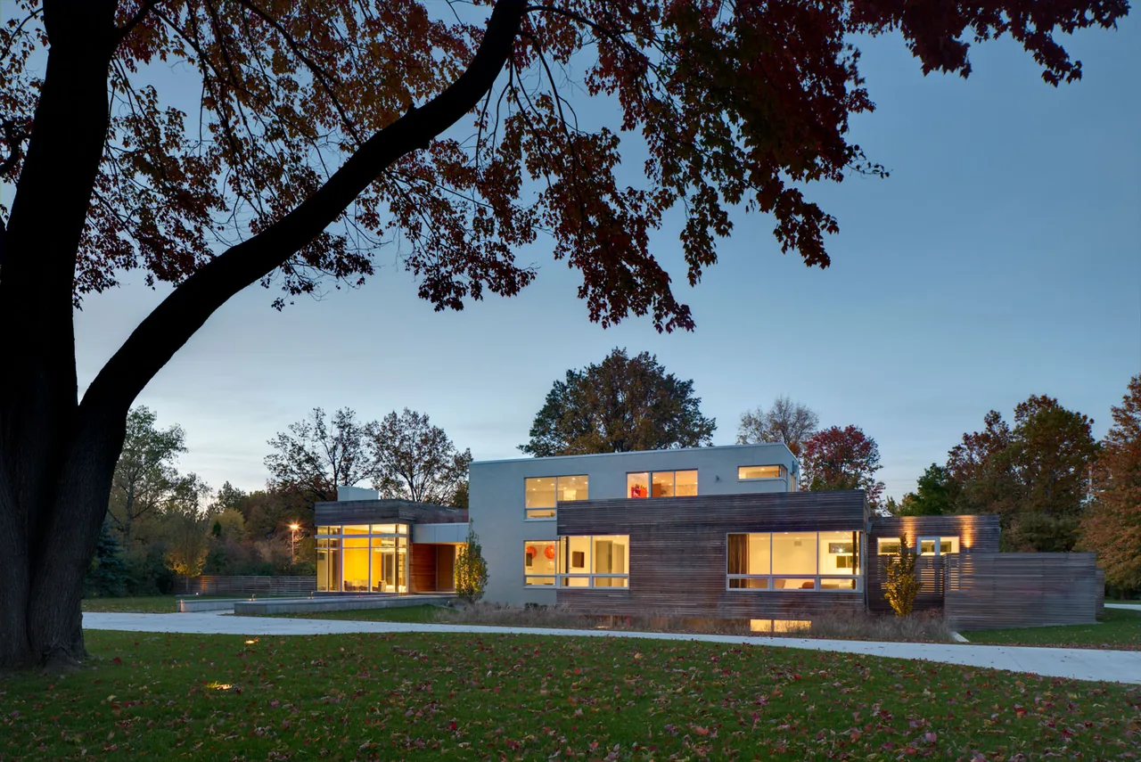 Exterior front view of the Shaker Heights Residence showing a mix of white stucco and wood siding under a clear sky at dusk.