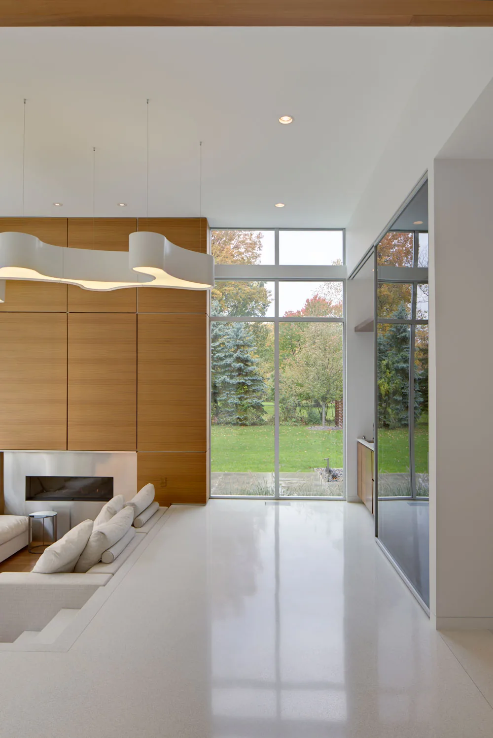 Living room with recessed seating area, wood panel fireplace wall, and expansive glass windows overlooking the yard.