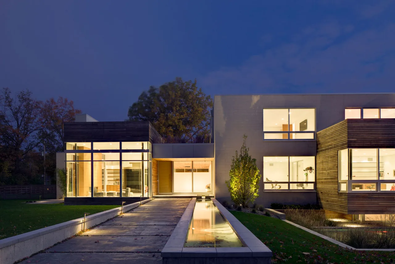 Exterior front view of contemporary residence with illuminated interiors and reflecting pool at dusk.