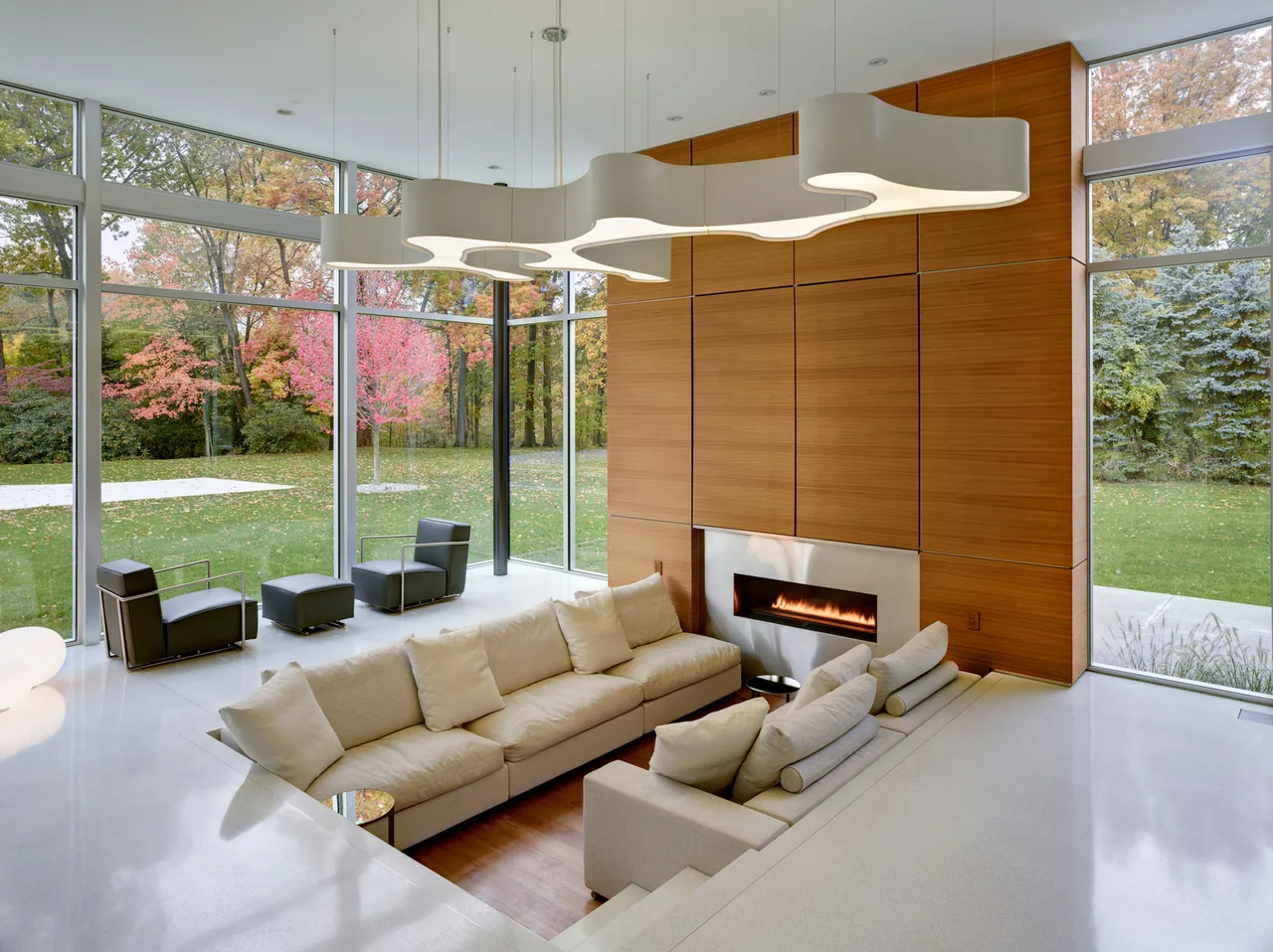 Living room with sunken seating area, floor-to-ceiling glazing, and a modern fireplace set in a wood-paneled wall.