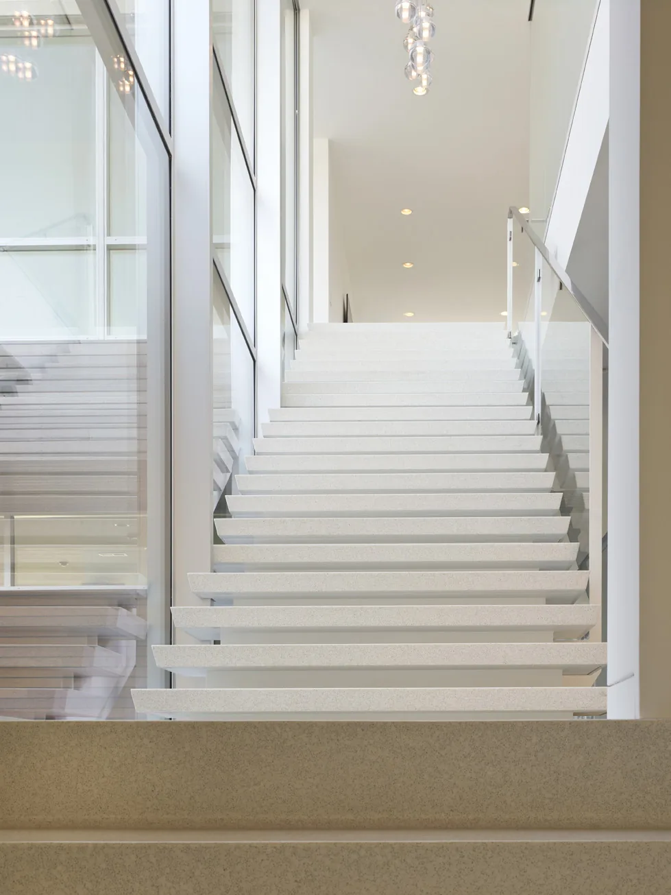 Floating staircase with glass railing beside a window wall in a modern interior.