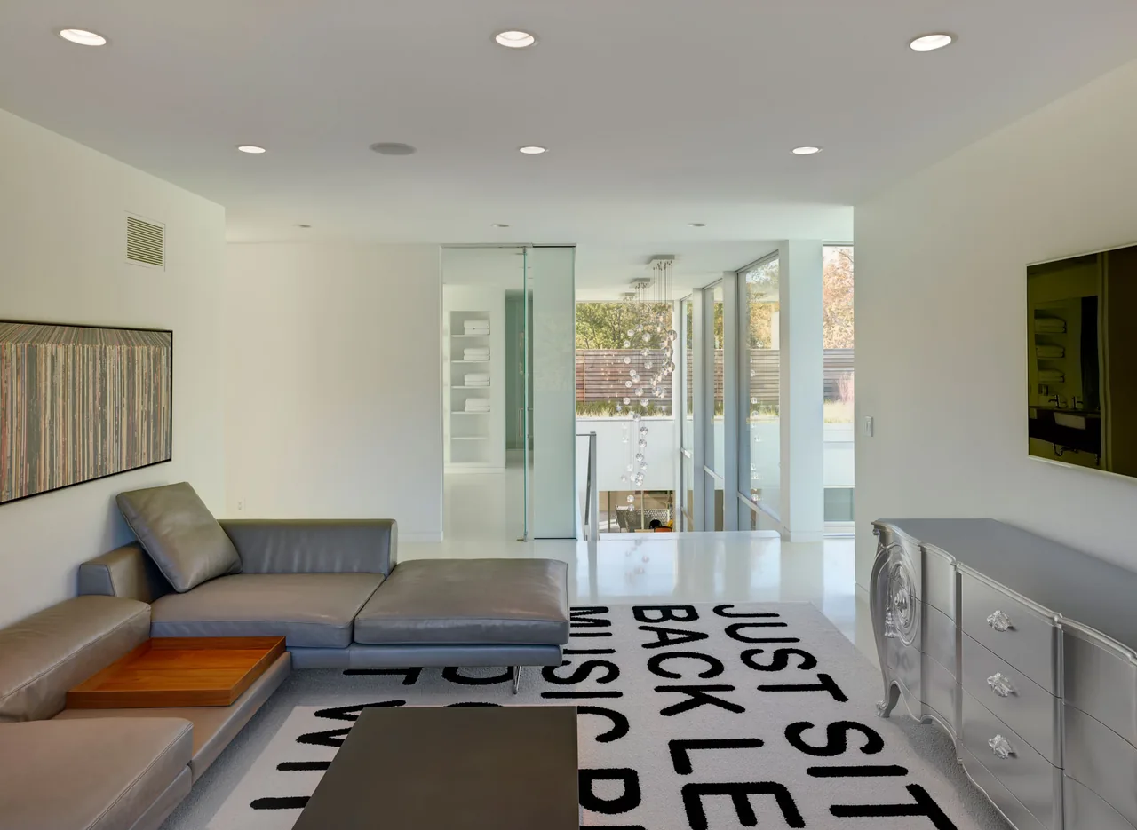 Living room in Shaker Heights Residence features a gray leather sectional, large text rug, and floor-to-ceiling glazing overlooking a stairwell.