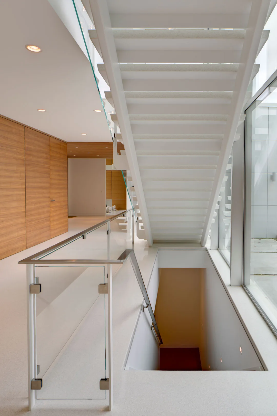 Floating white staircase with glass railing and large window wall in a modern interior space.