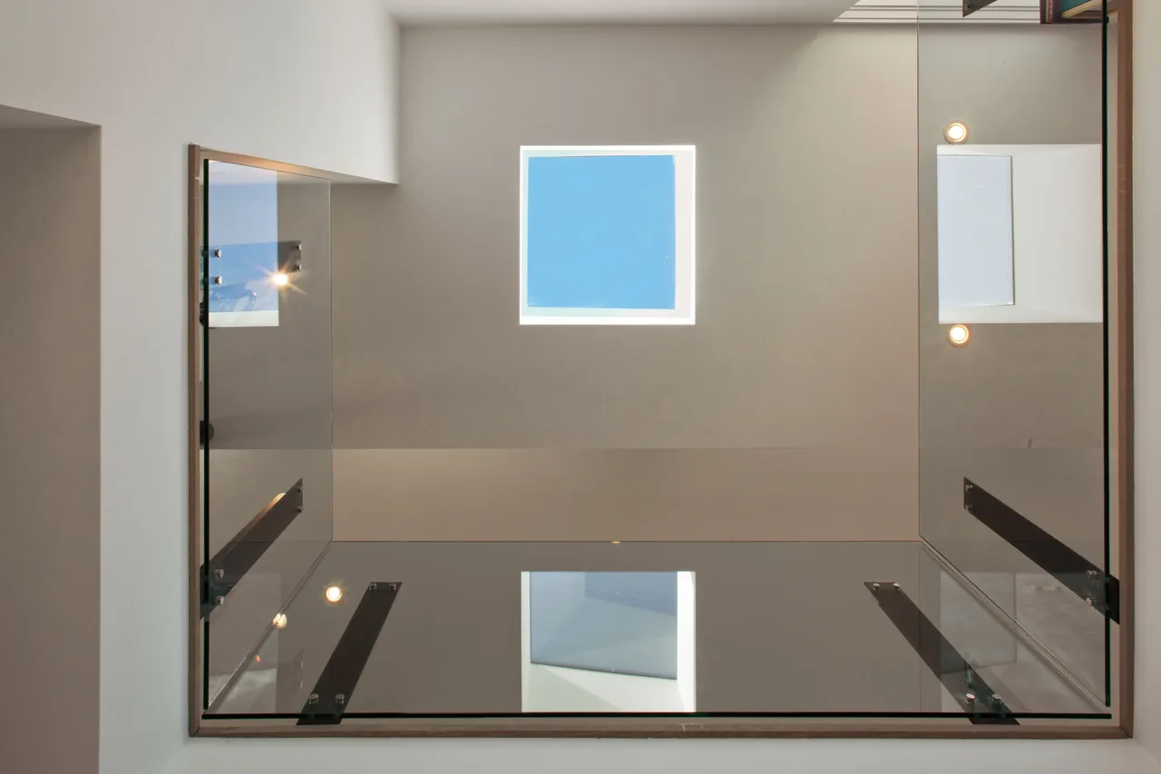 Square skylight with glass railing and recessed light fixtures around the opening.