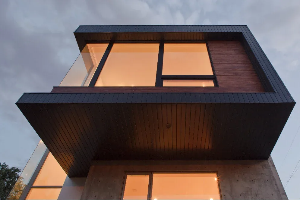 Exterior front view of a modern house featuring a cantilevered upper level with floor-to-ceiling glazing and wood siding.