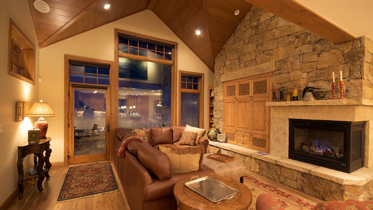 Interior view of a living room featuring a stone fireplace with built-in cabinets, leather seating, and floor-to-ceiling glazing.