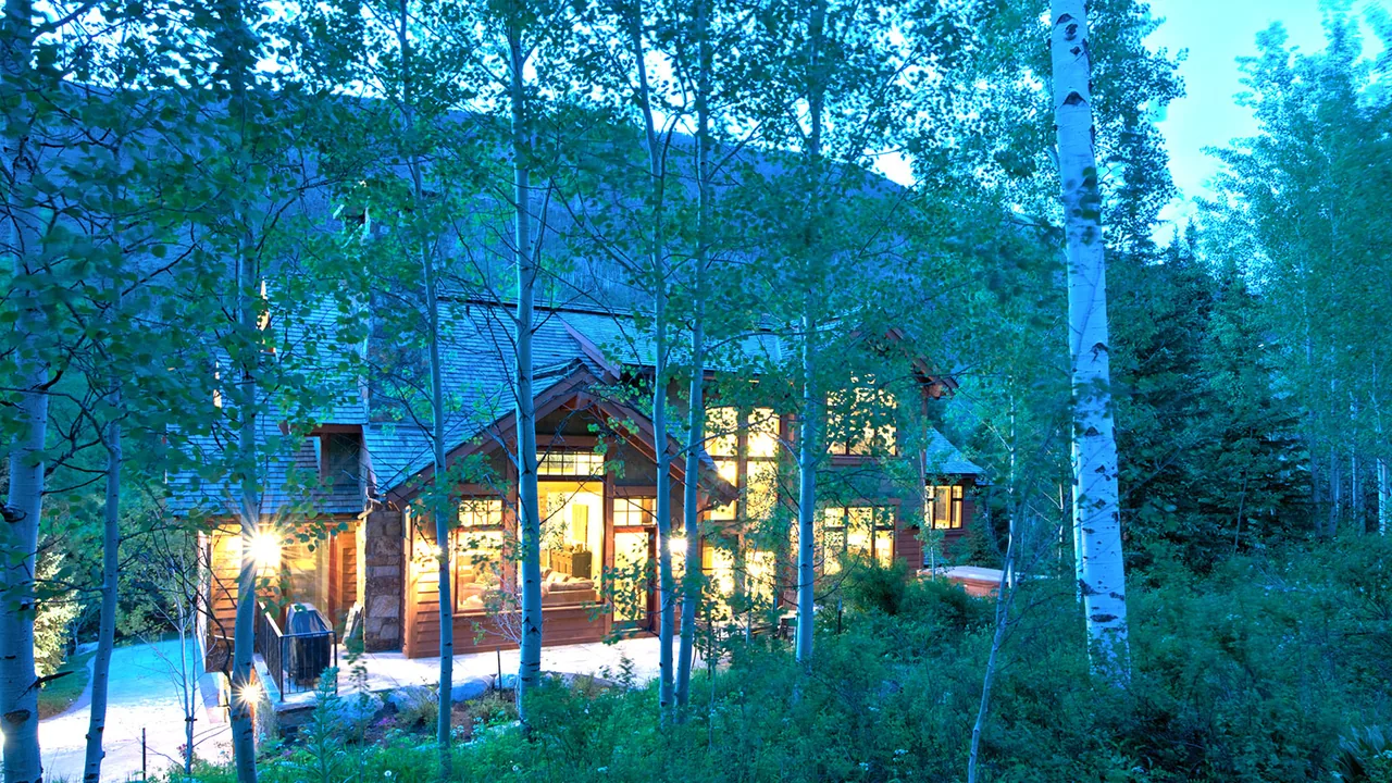 Dusk exterior view of a residence surrounded by trees with illuminated interior spaces.