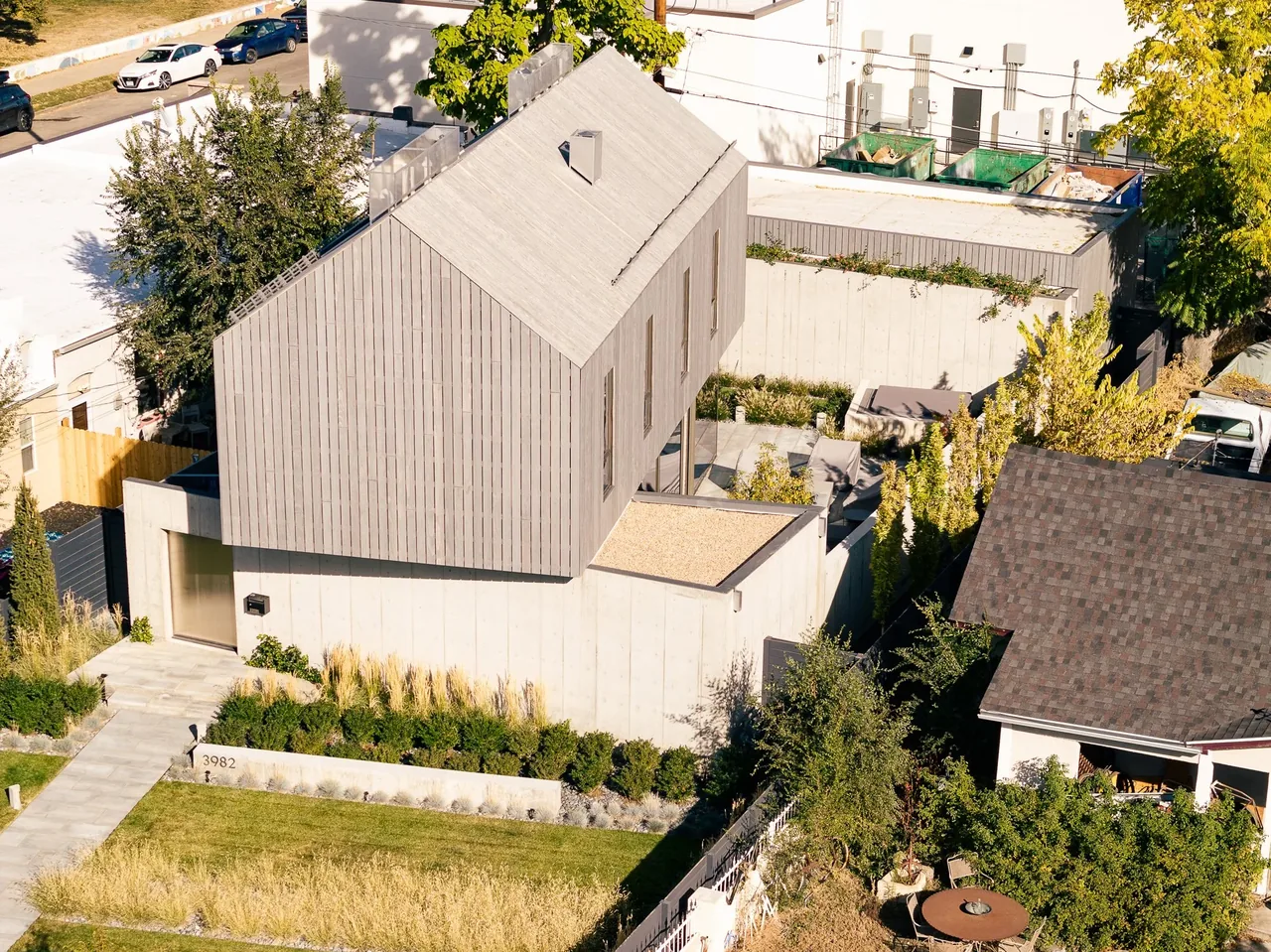 Modern two-story home with vertical wood siding and concrete base, featuring landscaping with low planters and tall grasses surrounding the property.