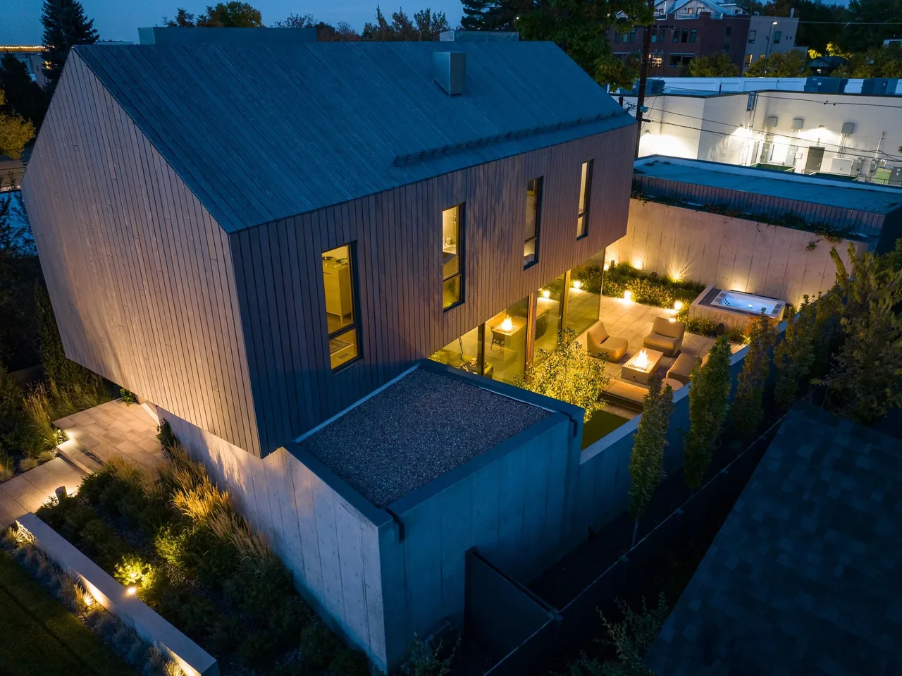 Night aerial photo of a two-story courtyard house with wood siding, concrete walls, and an illuminated outdoor patio area.