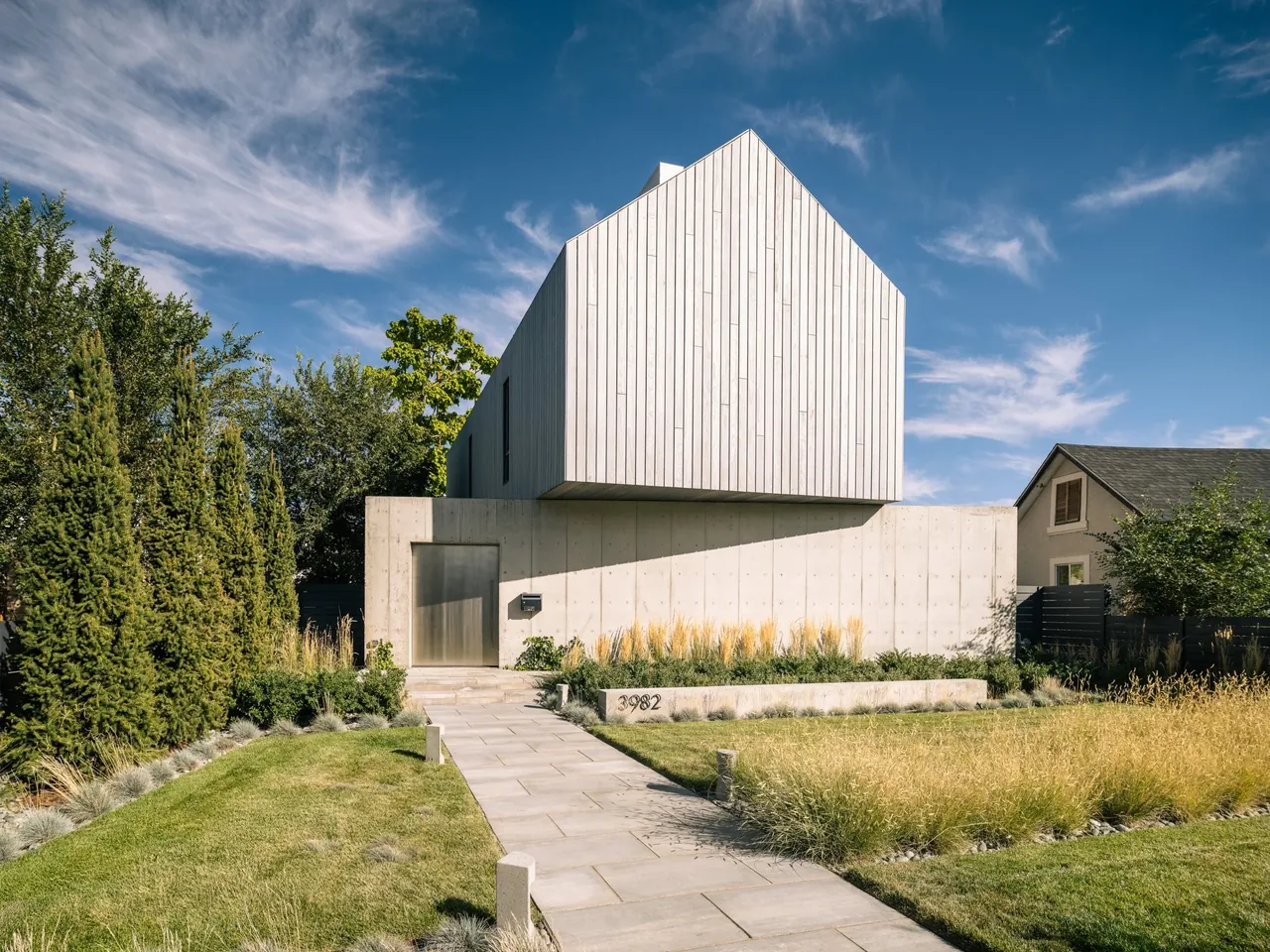 Front exterior of the Courtyard House showing a concrete base with a cantilevered wood-clad upper volume with a gable roof.