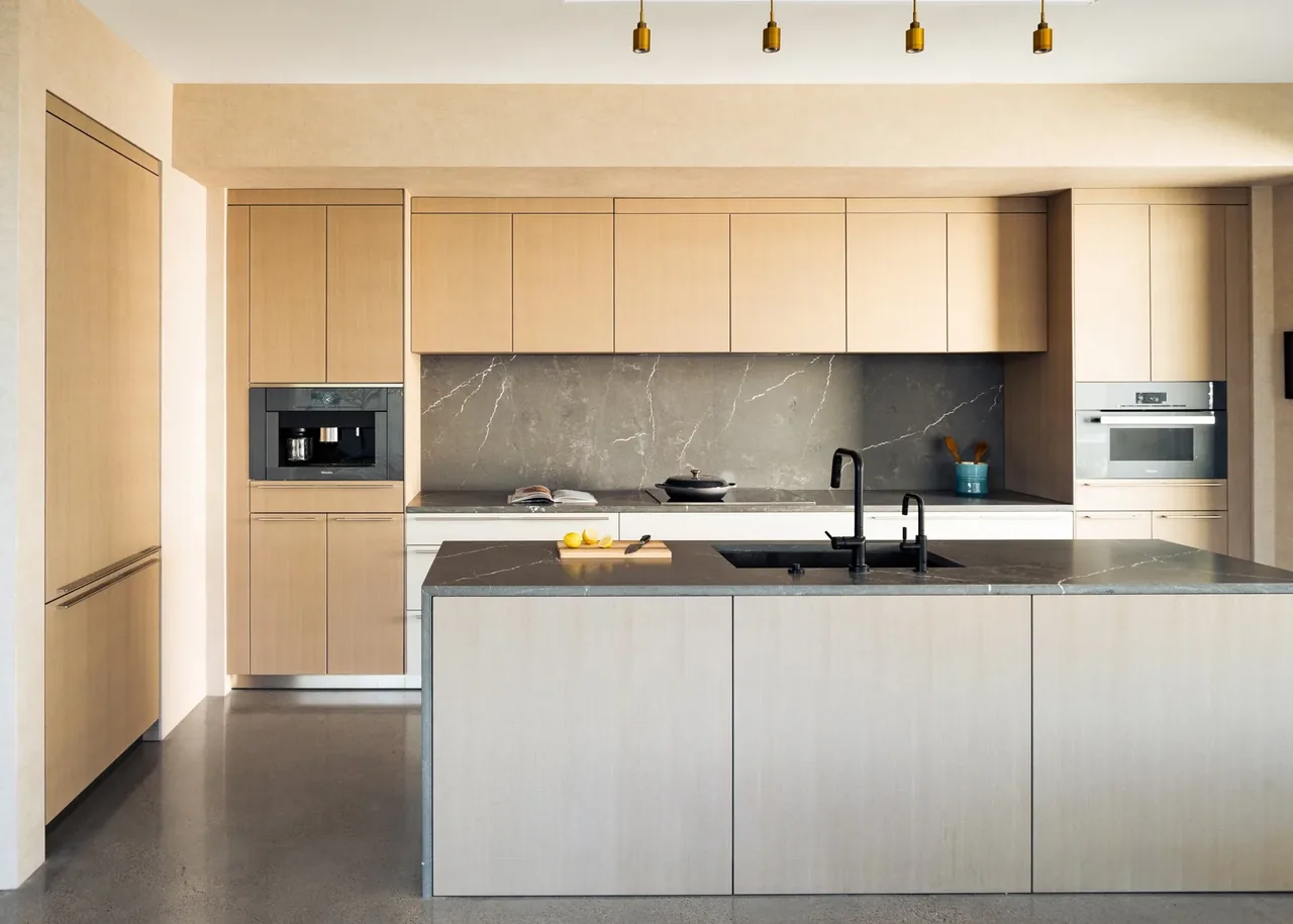 Kitchen with light wood cabinets, dark stone counters, and built-in coffee maker and oven.