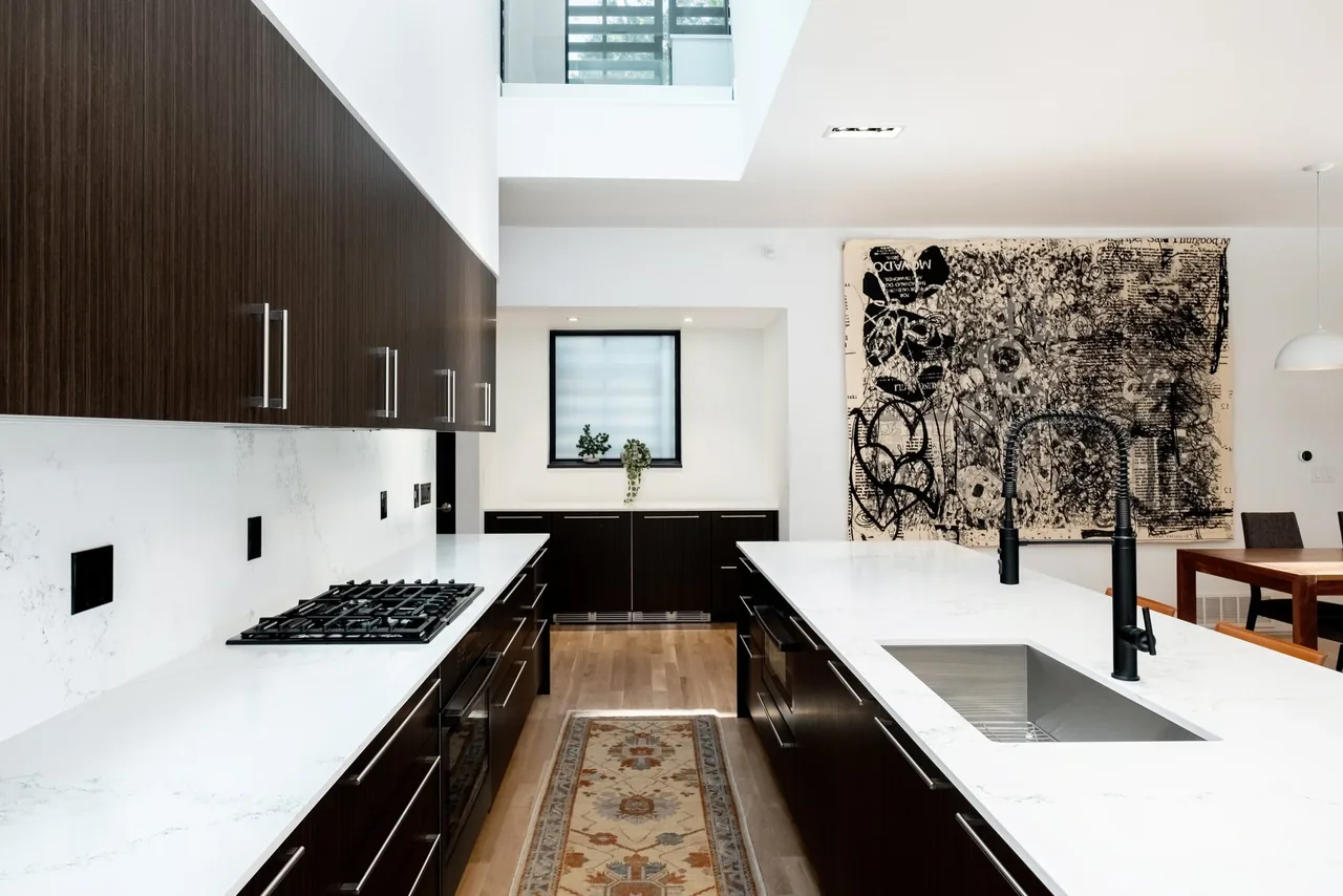 Kitchen interior featuring dark cabinetry, white marble countertops, and a central island with integrated sink and faucet.