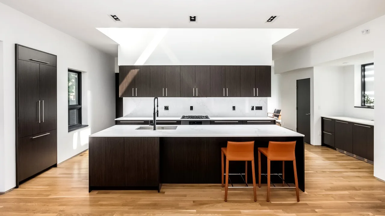 Kitchen features dark wood cabinetry with a central island and integrated appliances under a skylight