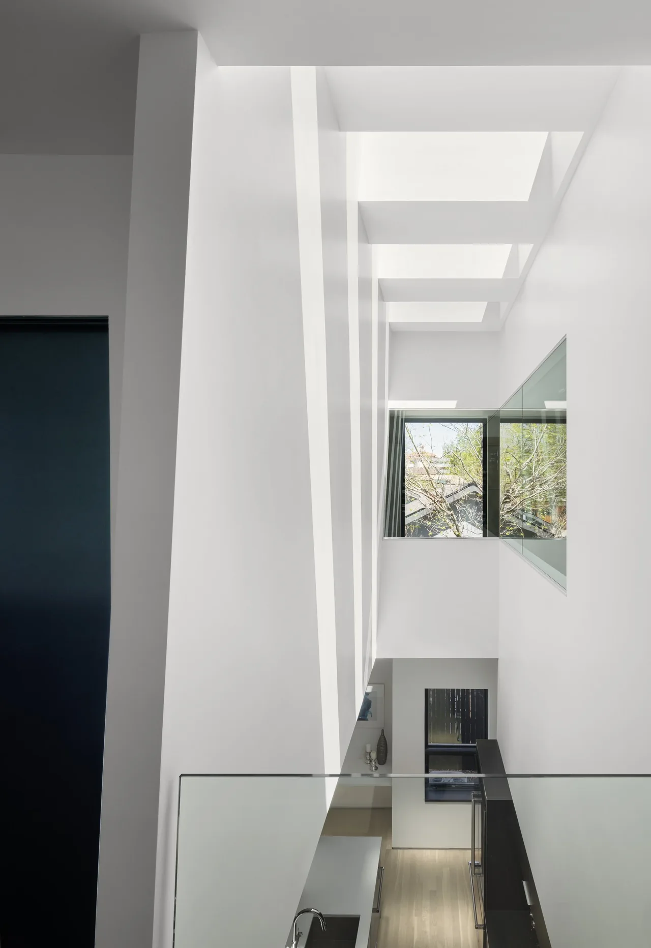 Vertical interior space features multiple rectangular skylights and glass railings overlooking a kitchen below.