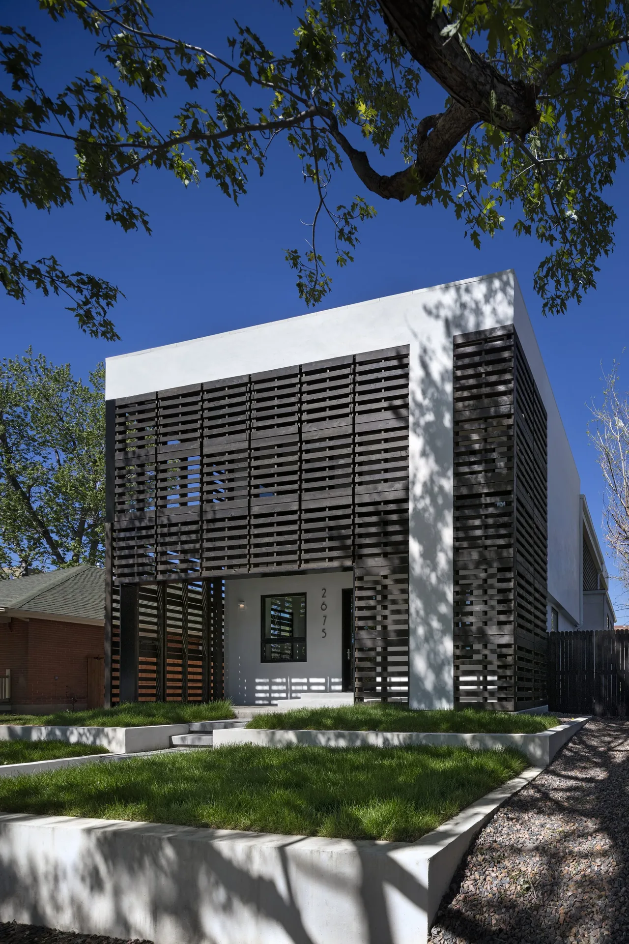 Exterior front view of a modern house featuring horizontal wooden slat screens over a white stucco facade.